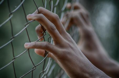 A young person's hands against a fence