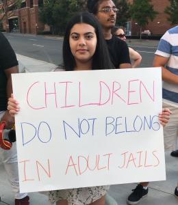 Young person holding poster reading Children do not belong in adult jails
