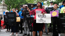 Protesters hold signs including one reading "Rikers = death"